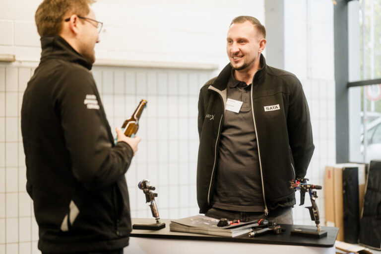 Zwei Mitarbeiter der Partnerfirma jetX stehen lachend an ihrem Stand auf einem Event von WerksKolleg.