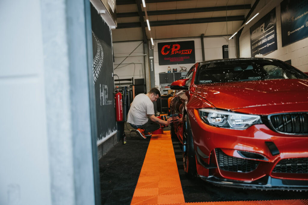 Junger Mann poliert die silbernen Felgen seines roten, sportlichen Autos