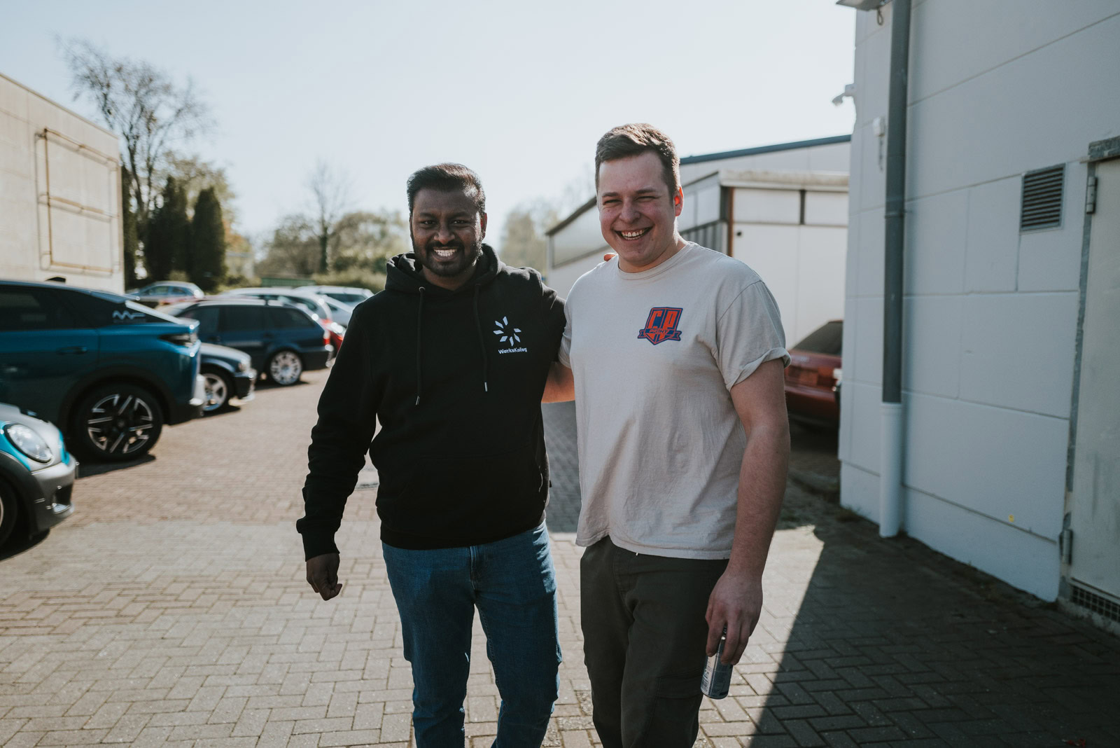 Ein Smart Repair Tutor und ein Kursteilnehmer stehen auf einem Parkplatz und lachen in die Kamera